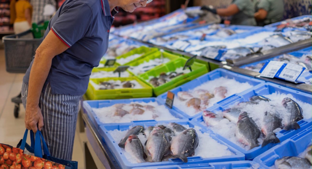 A shopper looks over trays of fresh whole fish on ice at a supermarket seafood counter.